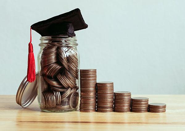 Piles of coins getting larger with grad hat on tallest.